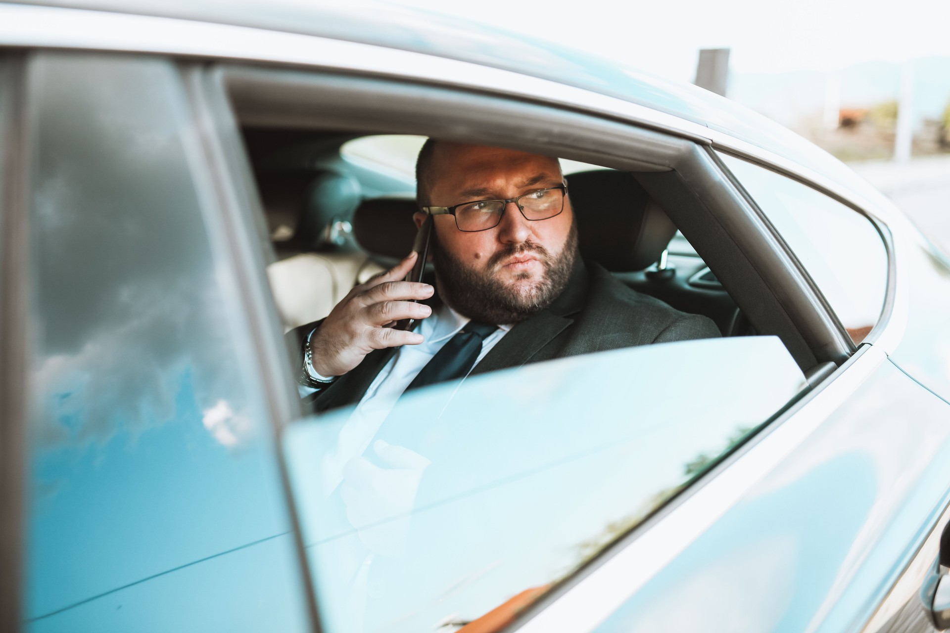 Middle Aged Businessman With Stern Face Talking On Smartphone While Traveling By Car